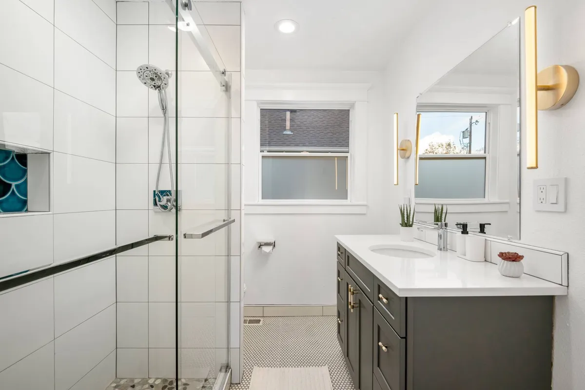 A bright, modern bathroom with a glass shower enclosure, double sink vanity, and stylish lighting fixtures. Natural light streams in, illuminating the space and highlighting the serene, fresh atmosphere.