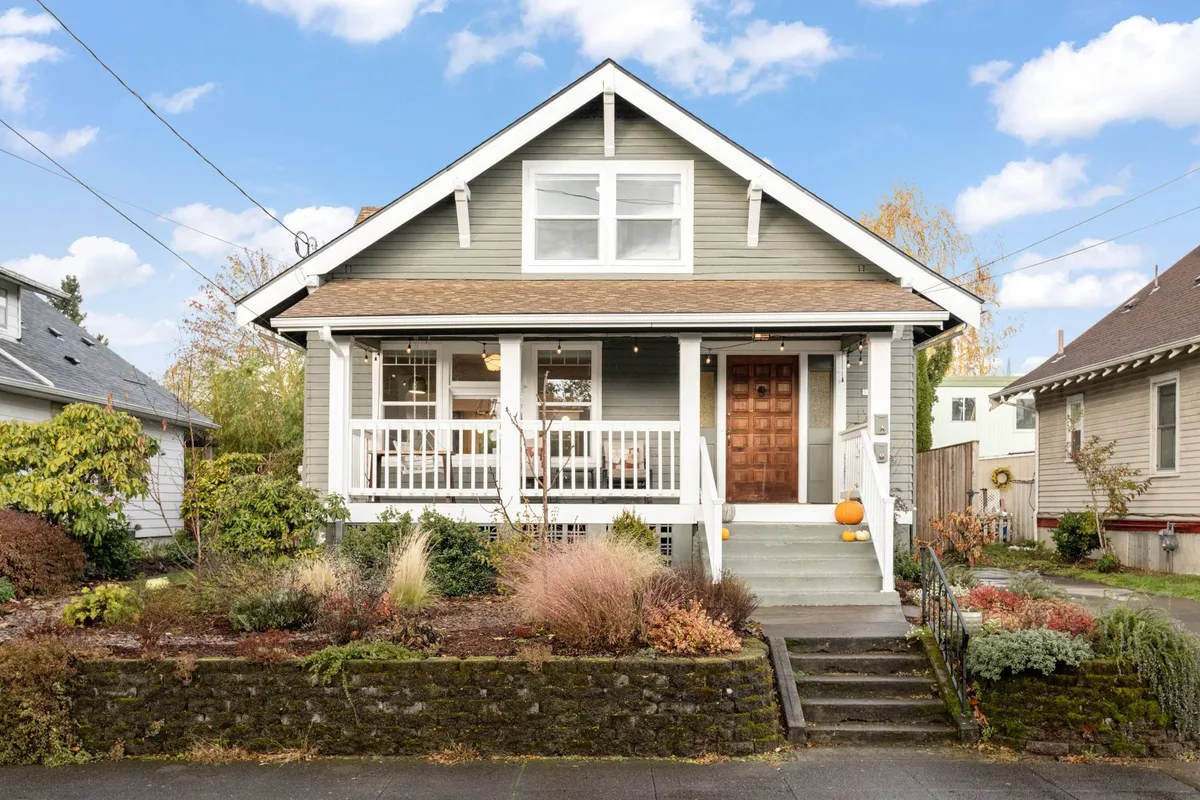 The image shows the inviting front porch of Rhone Retreat, complete with a wooden door, landscaped garden, and cozy porch seating. The outdoor space feels welcoming and is perfect for gathering with friends or enjoying quiet moments surrounded by greenery.