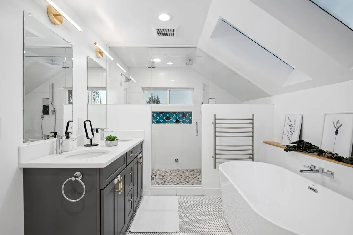 A bright, tranquil bathroom with a freestanding bathtub, dual vanity sinks, a walk-in shower with decorative tiles, and ample natural light from a skylight. The space feels luxurious and spa-like, promoting relaxation and self-care.