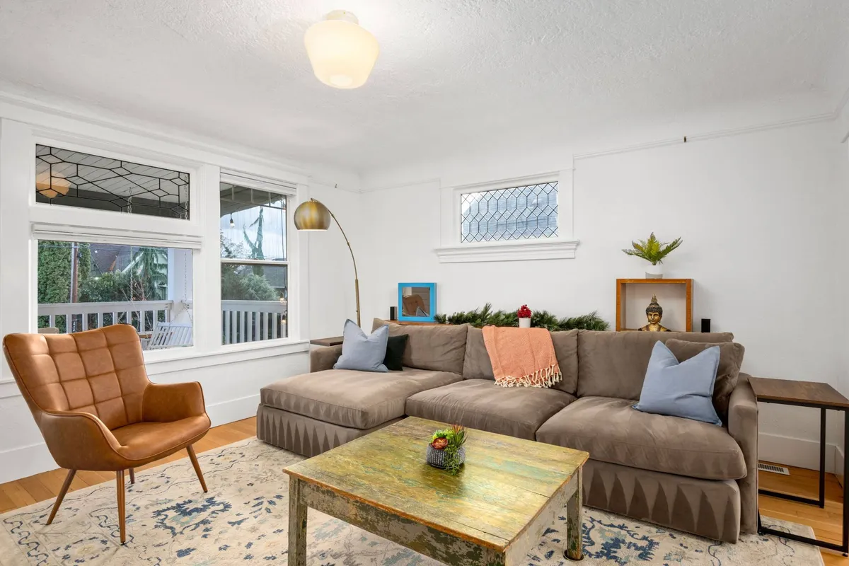 This inviting living room scene features a comfortable sectional sofa, a unique coffee table, a stylish armchair, lush decorative plants, and an artistic lamp. The arrangement encourages relaxation, conversation, and togetherness in a cozy yet spacious setting.
