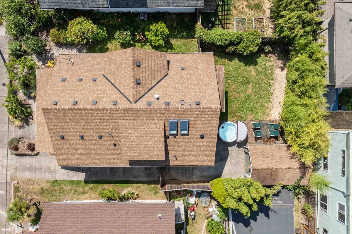 The image showcases the spacious backyard patio with a view of the pool area, distinctive roof design, and surrounding greenery. This outdoor oasis is perfect for gatherings, lounging, or enjoying meals together in the fresh air.