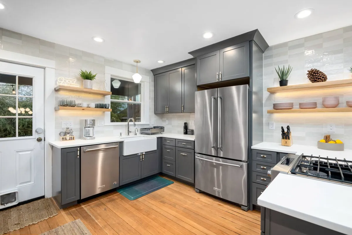 A modern chef's kitchen is the focal point here, featuring a stainless steel refrigerator, a spacious farmhouse sink, and open shelving decorated with plants. The setup is both highly functional and aesthetically pleasing, ideal for group meal prep and culinary creativity.