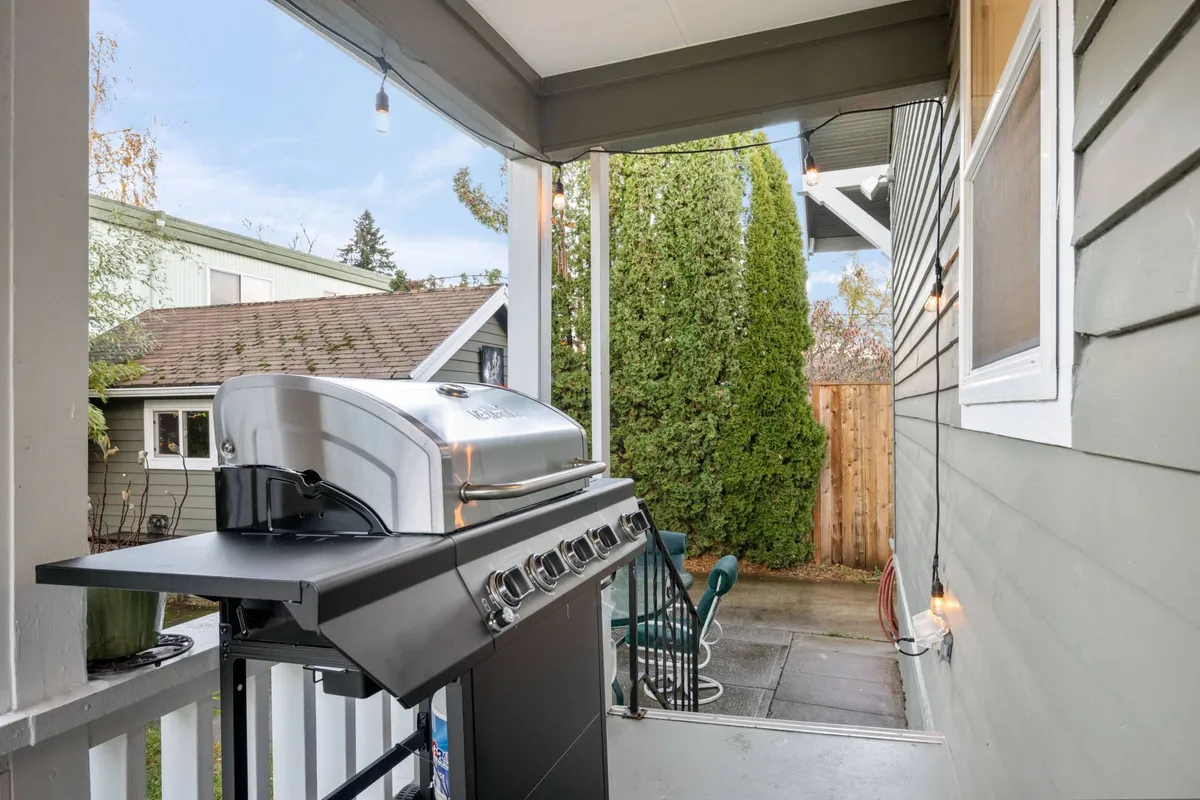This exterior shot zooms in on a well-appointed patio area with a grill, potted plant, greenery, and comfortable outdoor furniture. The grill is the centerpiece, perfect for alfresco feasts and casual get-togethers, while the surrounding greenery enhances the relaxed mood.