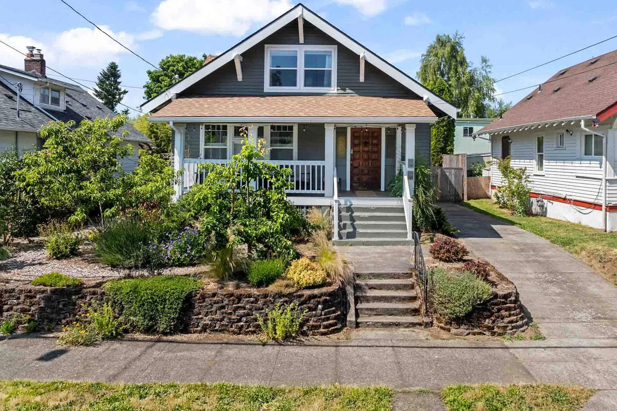 This image showcases the front exterior of a beautifully upgraded single-family house in Portland, Oregon. The inviting front porch is surrounded by a lush, landscaped garden, with steps leading warmly to the door. Soft sunset light bathes the scene, hinting at the perfect spot for a morning coffee or relaxing evening with loved ones.